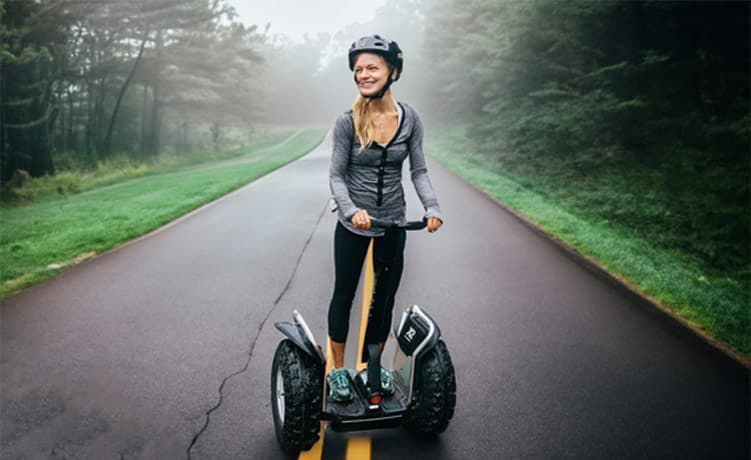 A girl riding a segway personal transportation device on a road in the woods